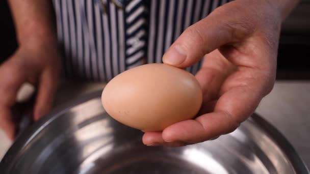 Las manos y un cuchillo de acero metálico rompen un huevo de gallina marrón y la yema cae en una sartén de metal. Primer plano
. - Metraje, vídeo