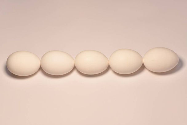 Five chicken eggs lined with a horizontal line in the center chain from top to bottom, left to right in a pinkish bed tone. - Foto, afbeelding