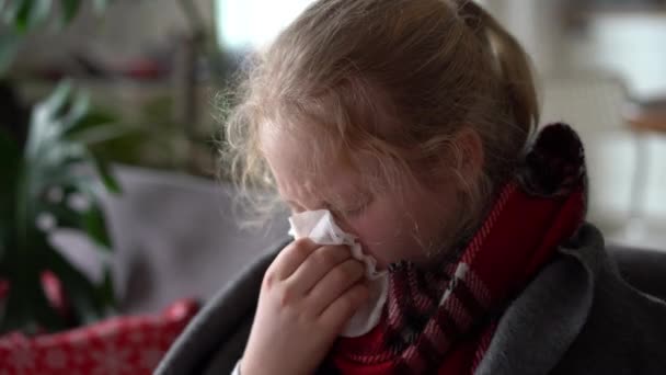 Kylmä valkoihoinen tyttö kotona. muotokuva sairas lapsi huivi ja ruudullinen sohvalla asunnossa, koulutyttö puhaltaa räkää lautasliinaan
 - Materiaali, video