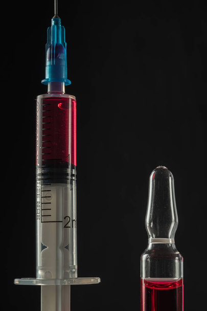 strzykawka i ampułka z czerwonym lekiem na ciemnym tle. Zbliżenie. Orientacja pionowa - Zdjęcie, obraz