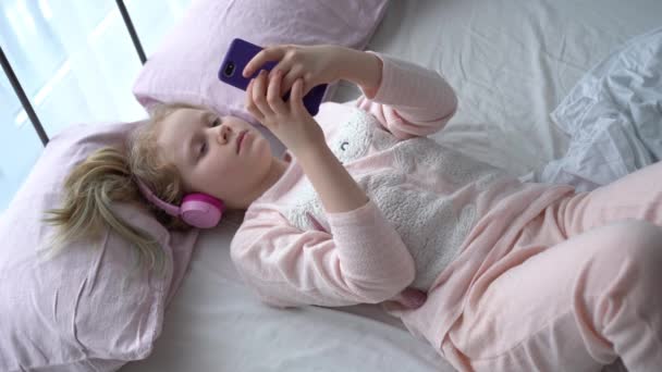 moderní život generace Z. dospívající dívka v pyžamu a sluchátka v místnosti na posteli poslouchá hudbu z chytrého telefonu. - Záběry, video