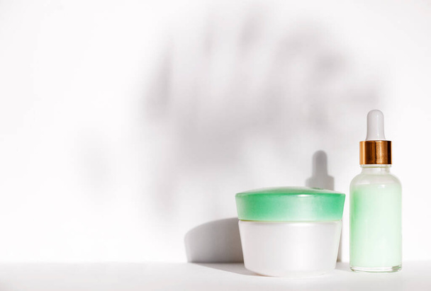 Natural cosmetics: serum with dropper and  cream jaron white background. Drop shadow from monstera leaf. Horizontal photo - Valokuva, kuva