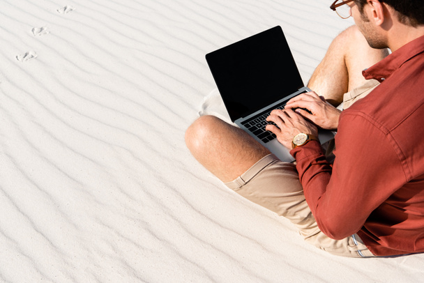 freelancer sitting on sandy beach with laptop against clear blue sky - Foto, afbeelding