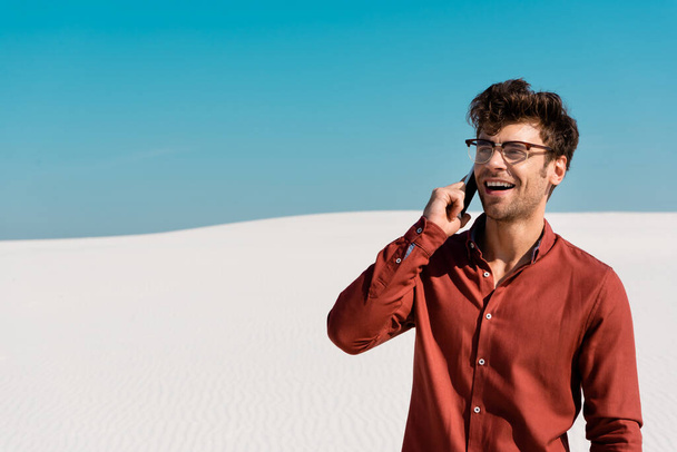 happy man on sandy beach talking on smartphone against clear blue sky - Photo, Image