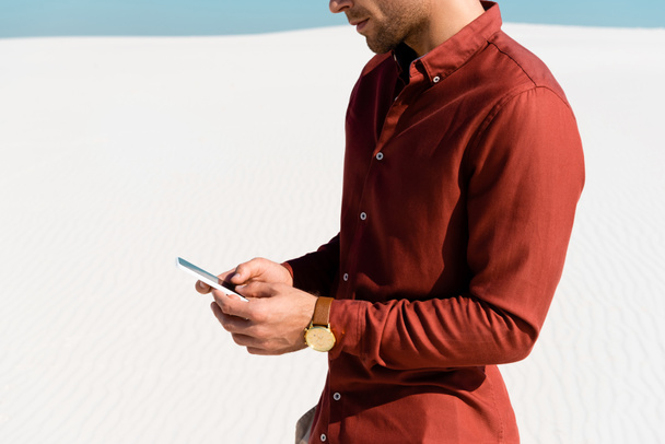 cropped view of man on sandy beach using smartphone - Foto, afbeelding