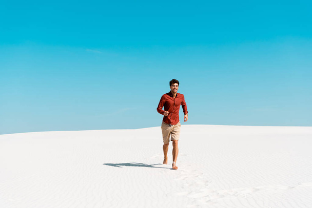 happy man running on sandy beach against clear blue sky - Фото, зображення