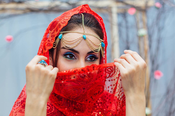 Beautiful eastern woman with makeup and jewelry wearing headscarf. - Фото, изображение