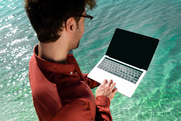 knappe freelancer met laptop staand in turquoise water - Foto, afbeelding