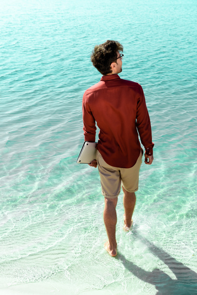back view of freelancer with laptop standing in turquoise water - Fotoğraf, Görsel