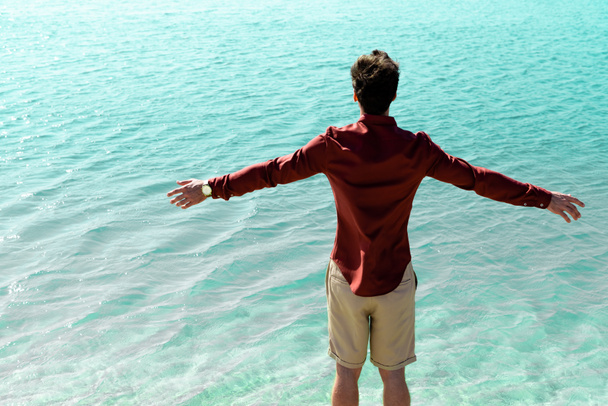 back view of man with outstretched hands standing in turquoise water - Foto, imagen