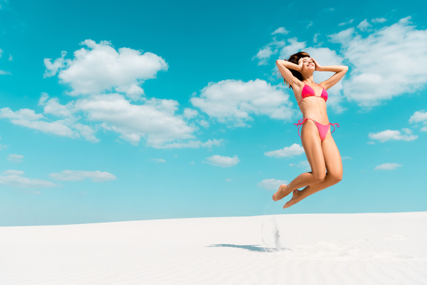 felice bella ragazza sexy in costume da bagno saltando sulla spiaggia di sabbia con cielo blu e nuvole
 - Foto, immagini