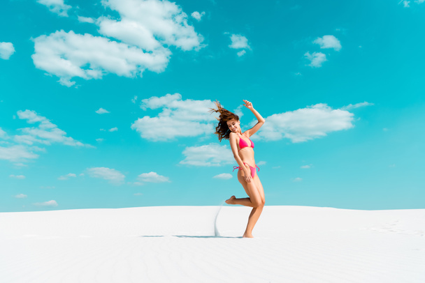 smiling beautiful sexy girl in swimsuit jumping on sandy beach with blue sky and clouds - Foto, imagen