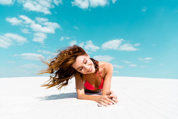 sonriente hermosa chica sexy en traje de baño acostado en la playa de arena con el cielo azul y las nubes en el fondo
 - Foto, imagen