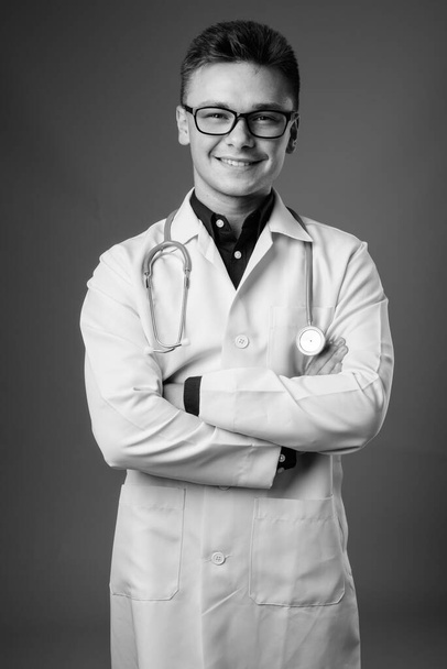 Студийный снимок молодого красивого врача в очках на сером фоне в черно-белом - Фото, изображение