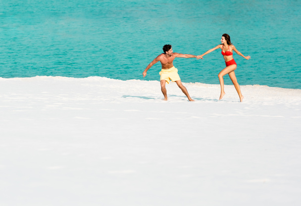 young sexy couple running on sandy beach near ocean - Foto, imagen