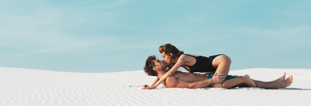 side view of sexy young woman kissing and lying on boyfriend on sandy beach, panoramic shot - Photo, Image