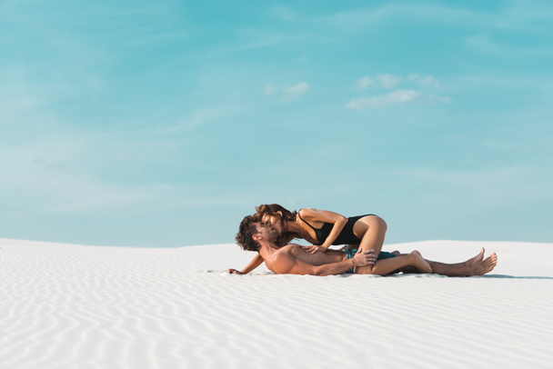 side view of sexy young woman kissing and lying on boyfriend on sandy beach - Foto, afbeelding