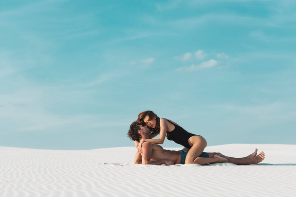 vista lateral de la mujer joven sexy sentado en el novio en la playa de arena
 - Foto, Imagen