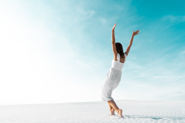 beautiful girl in white dress with hands in air on sandy beach with blue sky - Zdjęcie, obraz