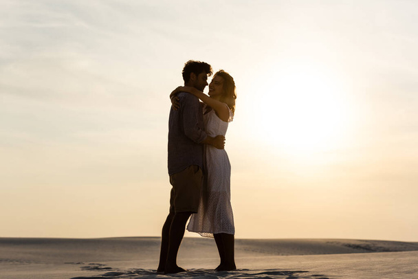 sivukuva nuoresta parista halaamassa hiekkarannalla auringonlaskun aikaan
 - Valokuva, kuva