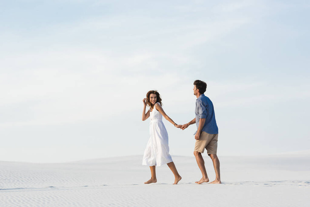 young couple walking on sandy beach and holding hands against blue sky - Foto, immagini