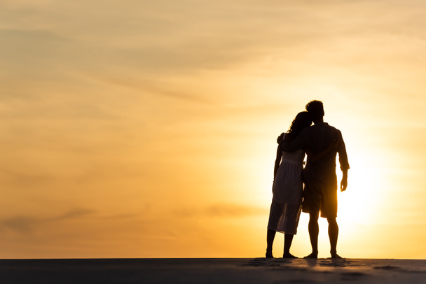 日没時に太陽とビーチで抱き合う男と女のシルエット - 写真・画像