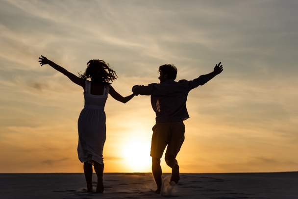 sagome di uomo e donna che corrono sulla spiaggia contro il sole durante il tramonto
 - Foto, immagini