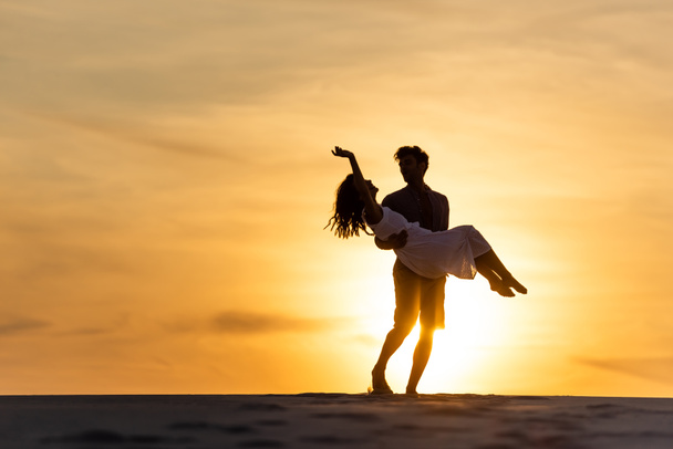 silhouettes of man spinning around woman on beach against sun during sunset - 写真・画像