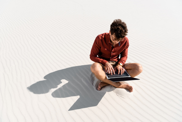 joven freelancer sentado en la playa de arena con portátil
 - Foto, imagen