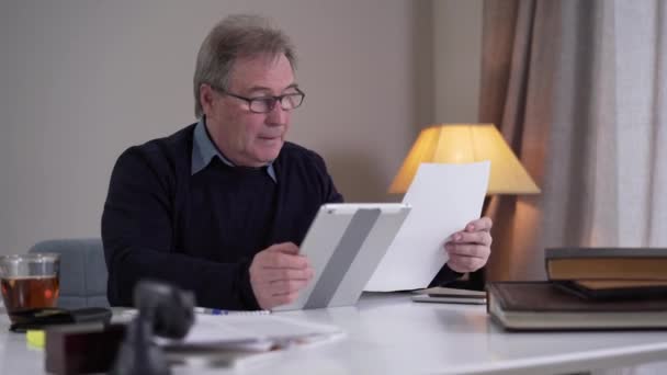 Stressed mature Caucasian businessman comparing information in documents and online and tearing papers. Anxious old man having business problems. Worry, lifestyle, anxiety, stress, business. - Materiał filmowy, wideo