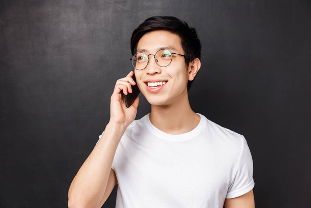 Technologie, zprávy a koncepce lidí. Detailní záběr portrét bezstarostného Asiata v brýlích, mluvení po telefonu, usmívání a odvracení pohledu při konverzaci, volání o schůzku - Fotografie, Obrázek