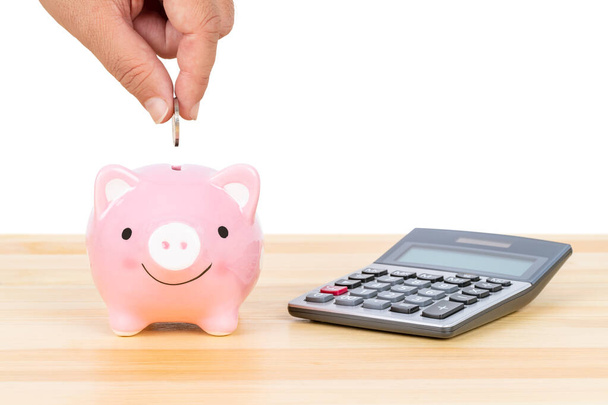 Piggy bank met de hand zetten insert munt en rekenmachine, op houten bureau, over witte achtergrond, sparen concept - Foto, afbeelding
