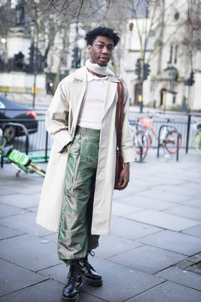 LONDON, UK- febryary 15 2020: Fashionable people on the street . Street style. A man in a long beige cloak, a neckerchief and green iridescent trousers poses - Фото, зображення