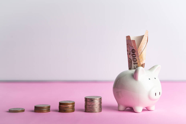 Concepto de ahorro y donación de dinero, dinero en una linda alcancía blanca en una mesa rosa
 - Foto, imagen