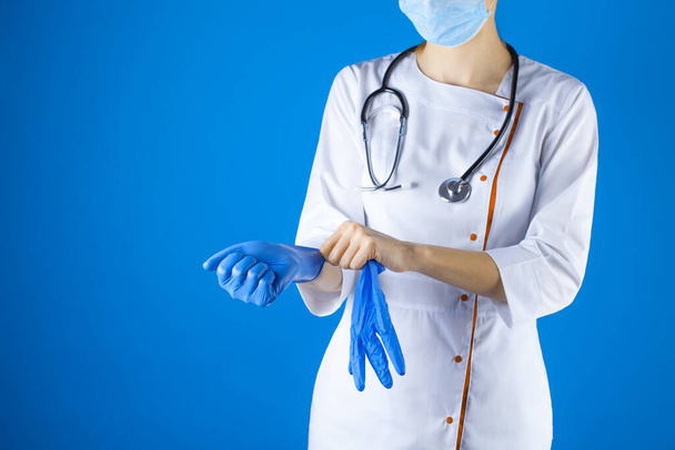 Female doctor in a white coat and mask wear gloves on his hands. Studio photo - Фото, зображення