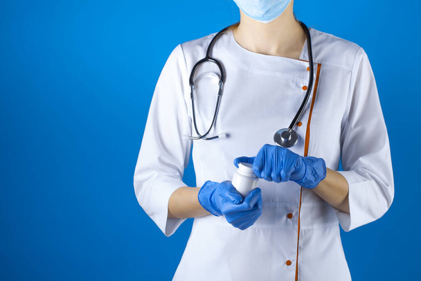 Vrouwelijke arts in een witte jas en masker met een experimentele tabletten in haar handen. Studiofoto - Foto, afbeelding