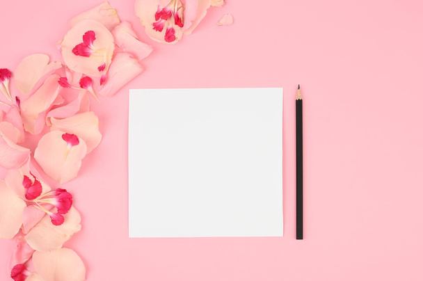Espacio de trabajo de bloguero plano o freelancer con una tarjeta de papel, pétalos rosa claro sobre un fondo de color
. - Foto, imagen