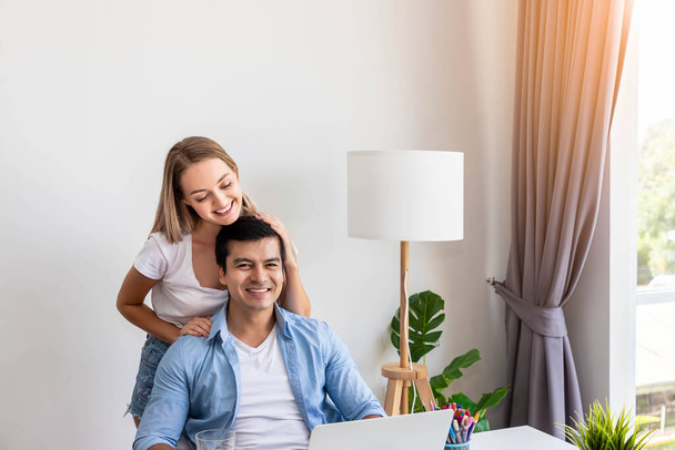 Férfi férj dolgozik otthon számítógép notebook, míg a nő felesége szolgálja narancslé és átöleli őt, nézi a kamera - Fotó, kép
