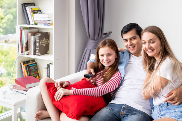 Šťastná rodina na gauči v obývacím pokoji, včetně otce, matky a dcery, si užívají sledování televize společně, s dálkovým ovládáním - Fotografie, Obrázek