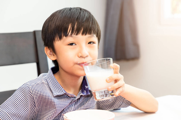 Adorável jovem asiático feliz tomando café da manhã e bebendo leite em casa pela manhã; olhando para a câmera
 - Foto, Imagem