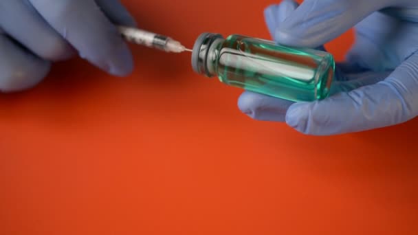 Doctors hands in blue gloves picks up a coronovirus COVID-19 vaccine in a syringe on a red background - Кадры, видео