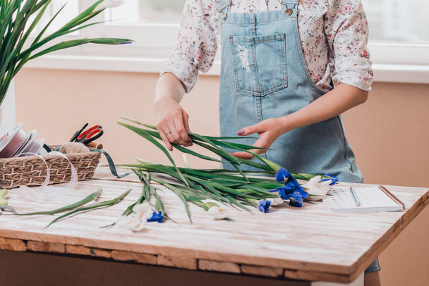 Hände einer jungen Floristin, die mit frischen Blumen arbeitet und einen Strauß Fleur-de-lises auf den Tisch zaubert. - Foto, Bild