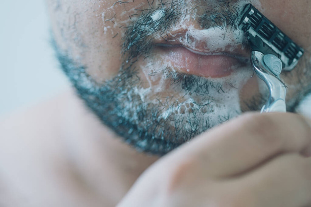 A férfi reggel borotválja az arcát a fürdőszobában. Közelről. - Fotó, kép
