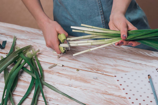 Руки молодої жінки-флориста, що працюють зі свіжими квітами, роблять букет з бліндажів на столі
. - Фото, зображення