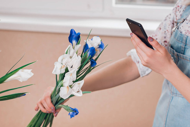 Young woman florist taking pictures of fresh flowers of fleur-de-lises on smartphone. Creative concept. - Fotografie, Obrázek