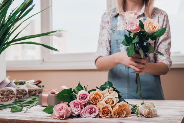 Kädet nuori nainen kukkakauppias työskentelevät tuoreita kukkia joten kukkakimppu vaaleanpunainen ruusuja pöydälle. Sulje se.
. - Valokuva, kuva