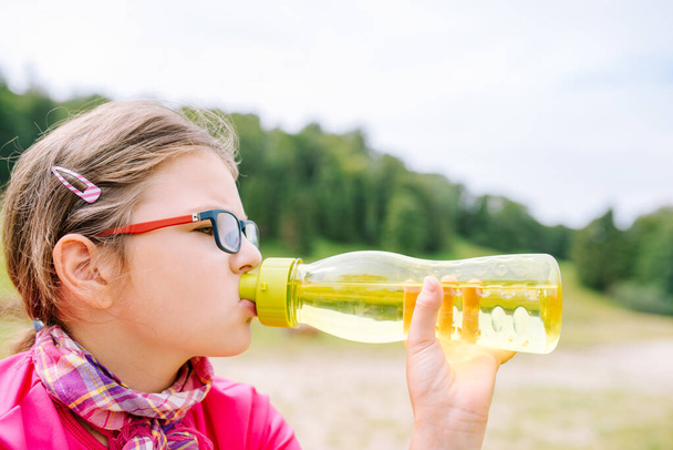 Menina com copos de água potável de uma garrafa de água verde durante uma viagem nas montanhas
 - Foto, Imagem