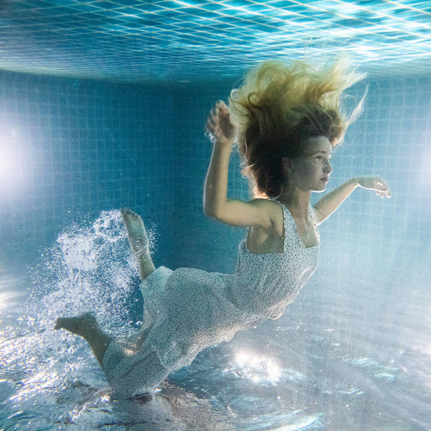 Красивая женщина с длинными рыжими волосами позирует под водой в белом платье
 - Фото, изображение