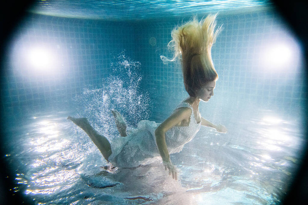 Hermosa mujer con el pelo largo y rojo posando bajo el agua en vestido blanco
 - Foto, Imagen