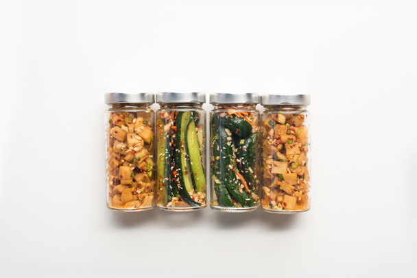 bovenaanzicht van komkommer en daikon radijs kimchi in potten op witte achtergrond - Foto, afbeelding